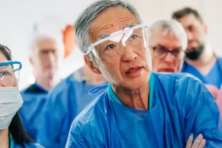 Ärzteteam in blauen Schutzkitteln und medizinischer Schutzbrille in einem Krankenhaus