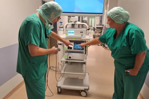 Zwei medizinische Fachkräfte in grüner OP-Kleidung bedienen ein medizinisches Gerät mit Touchscreen in einem Krankenhausflur