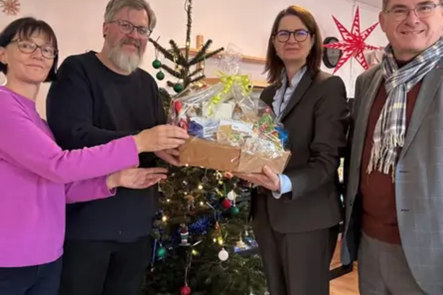 Vier Personen übergeben vor einem geschmückten Weihnachtsbaum einen Geschenkkorb