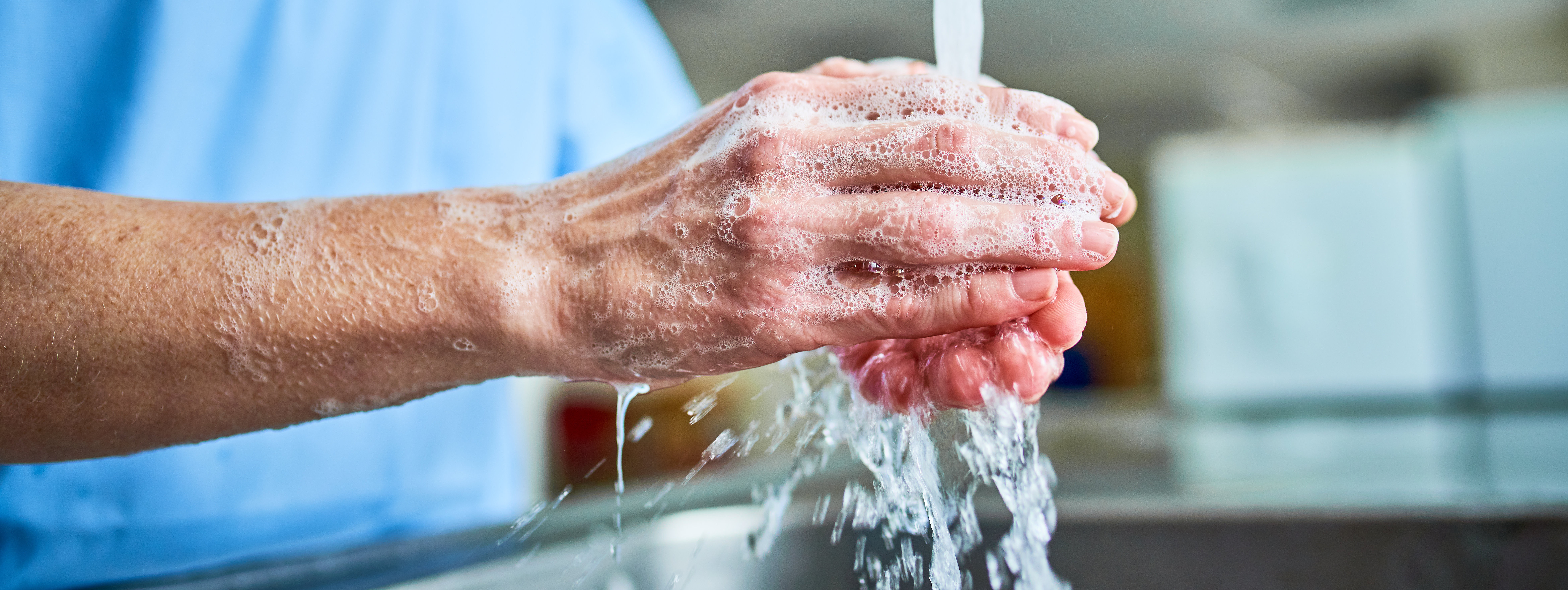 Hände werden unter fließendem Wasser mit Seifenschaum gewaschen.