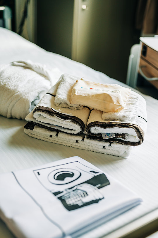 Gefaltete Handtücher und ein Stapel Stoffe liegen auf einem weißen Bett