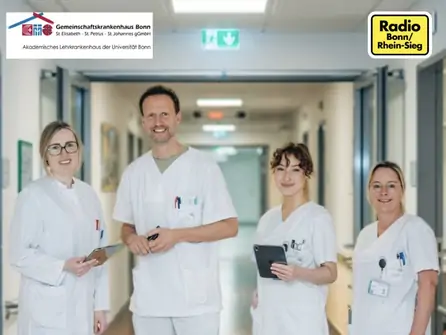 Vier medizinische Fachkräfte in weißen Kitteln stehen in einem Krankenhausflur und halten digitale Geräte