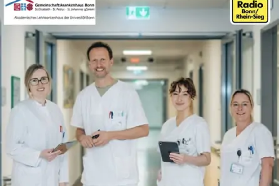 Vier medizinische Fachkräfte in weißen Kitteln stehen in einem Krankenhausflur und halten digitale Geräte