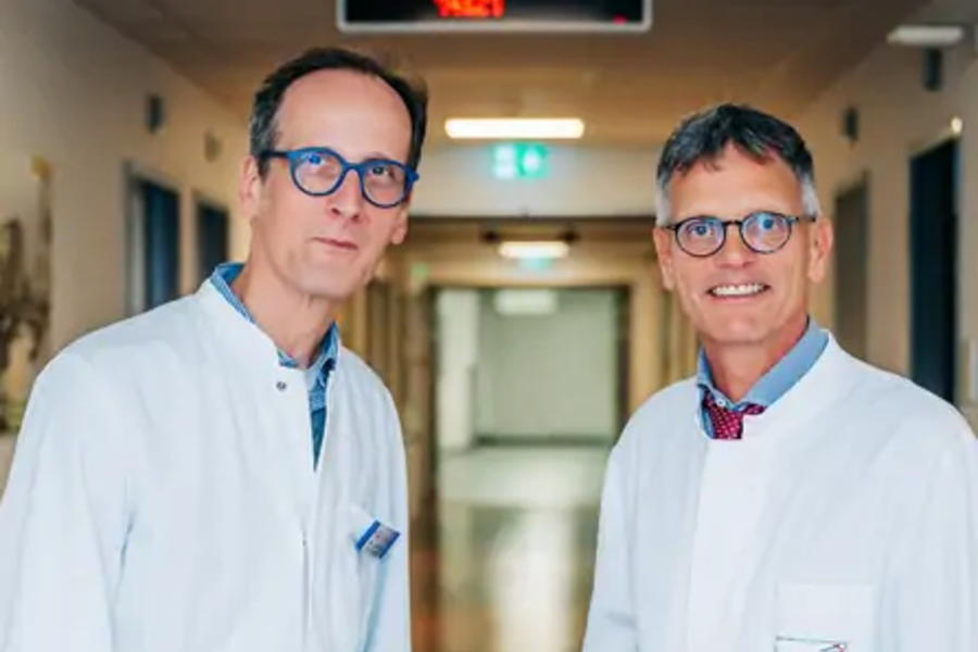 Zwei Männer in weißen Kitteln stehen in einem Krankenhausflur mit beleuchtetem Notausgangsschild im Hintergrund