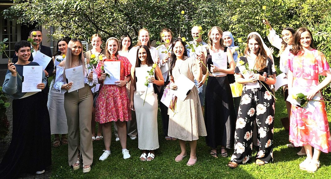 Gruppe von jungen Erwachsenen steht im Garten, hält Urkunden und Blumen, feiert Abschluss oder Auszeichnung