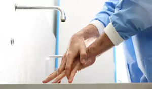 Person in blauem Schutzanzug wäscht Hände unter Wasserhahn