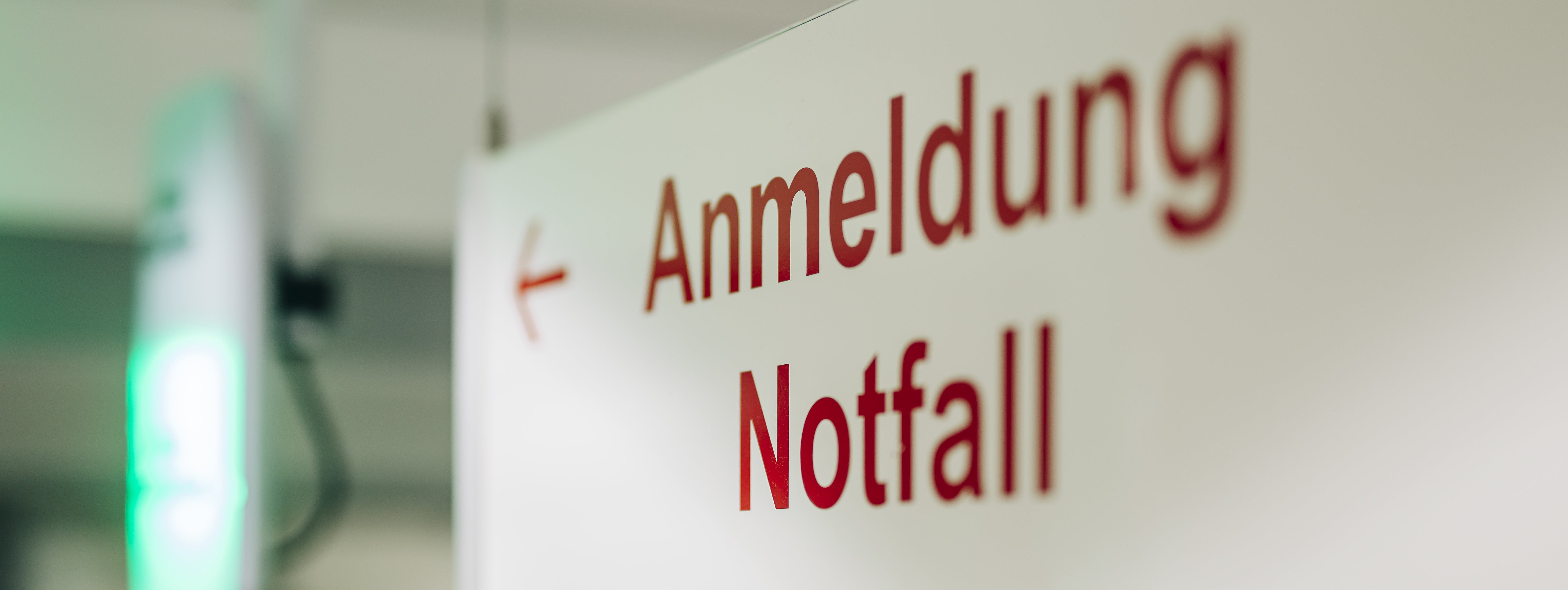 Schild mit roter Aufschrift 'Anmeldung Notfall' und einem Pfeil nach links in einem Flur