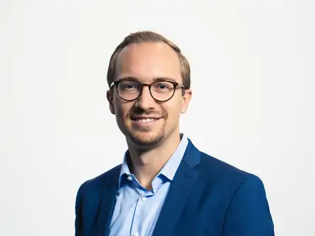 Herr Heistermann trägt einen blauen Anzug und ein hellblaues Hemd. Er steht in einer neutralen Pose.