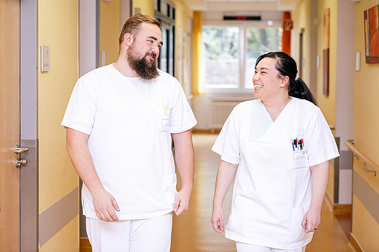 Zwei Pflegekräfte in weißen Kitteln gehen gemeinsam einen Krankenhausflur entlang
