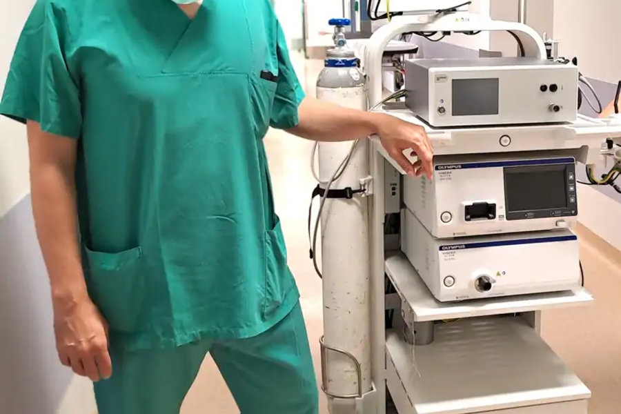 Medizinische Fachkraft in grüner OP-Kleidung steht neben einem medizinischen Gerät mit Monitor und mehreren Steuergeräten auf Rollen