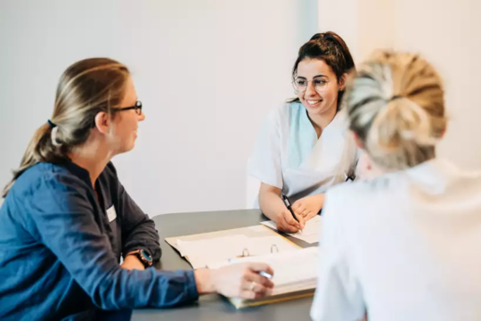 Drei Personen sitzen an einem Tisch und führen ein Gespräch