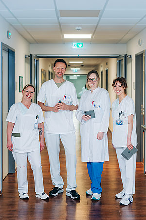 Vier medizinische Fachkräfte in weißer Arbeitskleidung stehen in einem Krankenhausflur, zwei halten Tablets