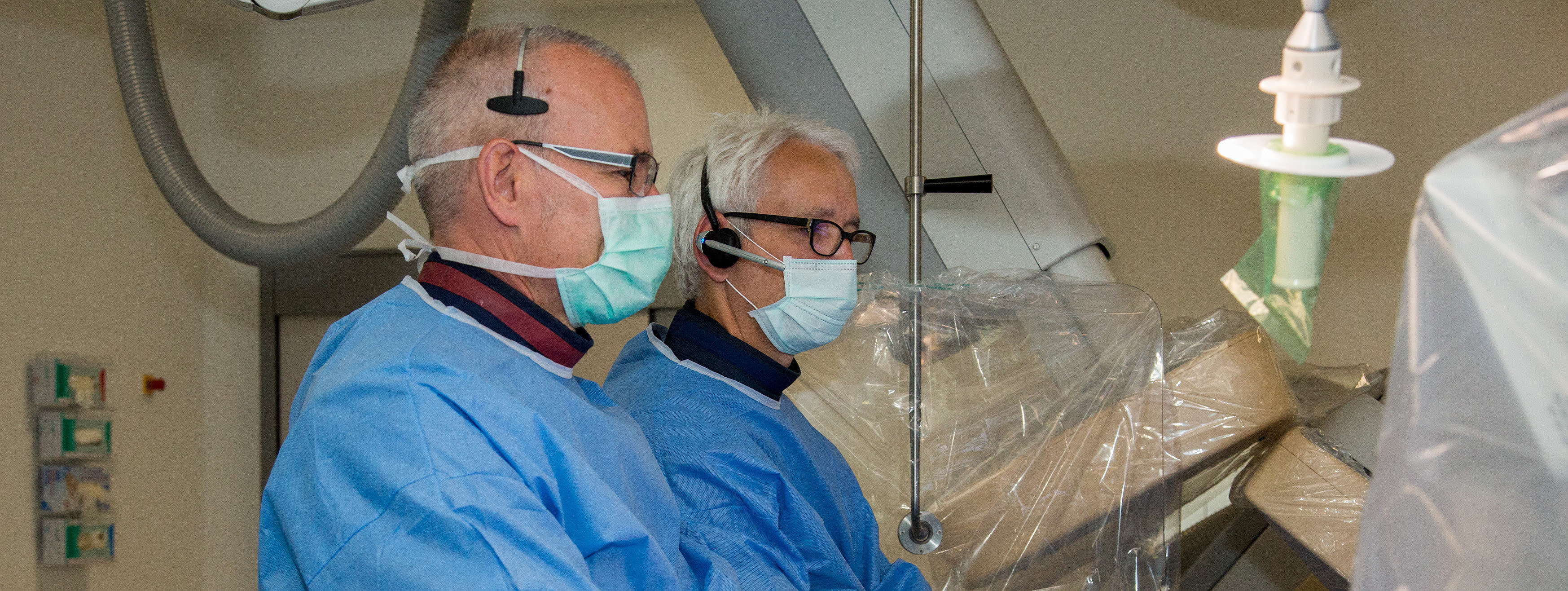 Zwei Personen in blauen OP-Kitteln und Handschuhen bedienen medizinische Geräte in einem Behandlungsraum.
