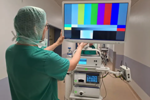 Medizinisches Personal in OP-Kleidung stellt Monitor mit Farbtestbild auf medizinischem Gerät im Krankenhausflur ein