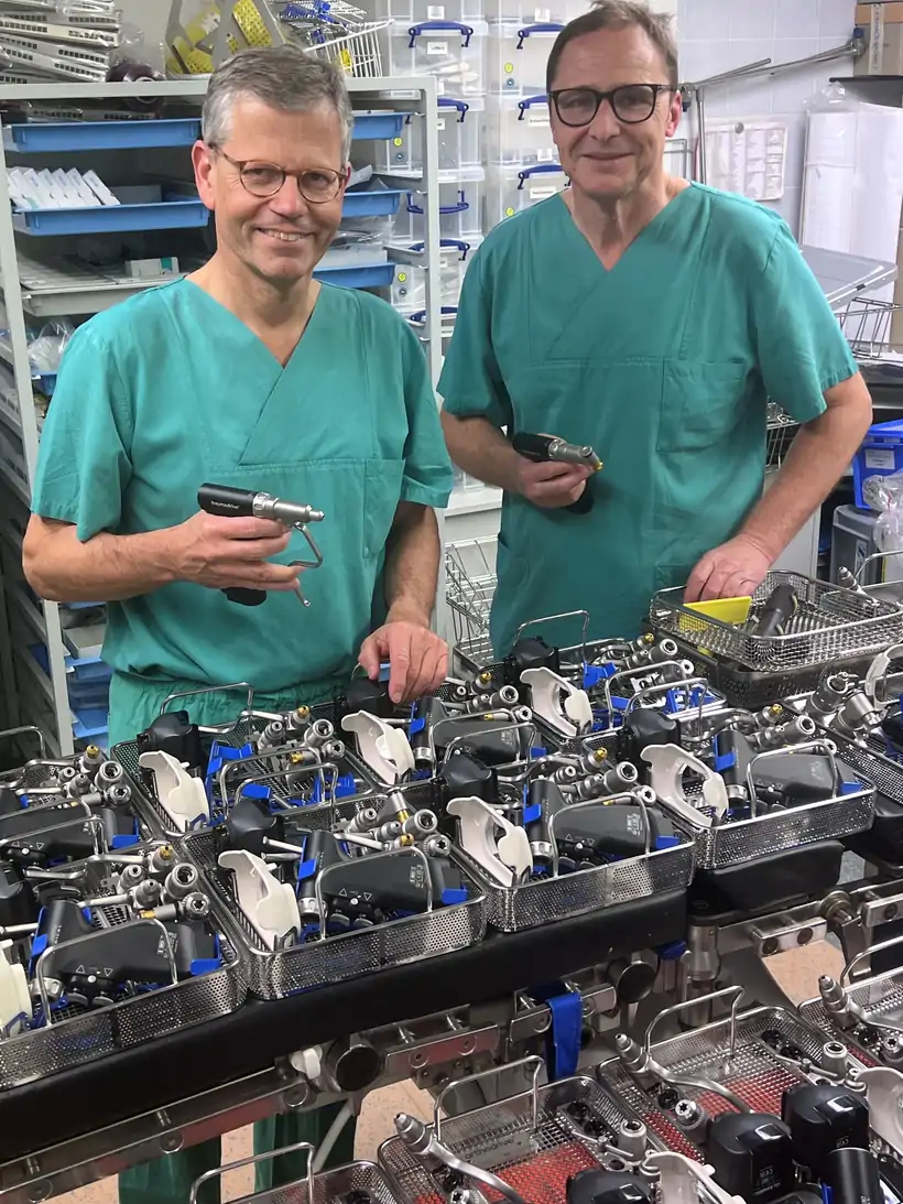 Zwei Personen in grünen OP-Kitteln arbeiten an einer Montage von medizinischen Geräten mit Werkzeugen in einer Werkstatt