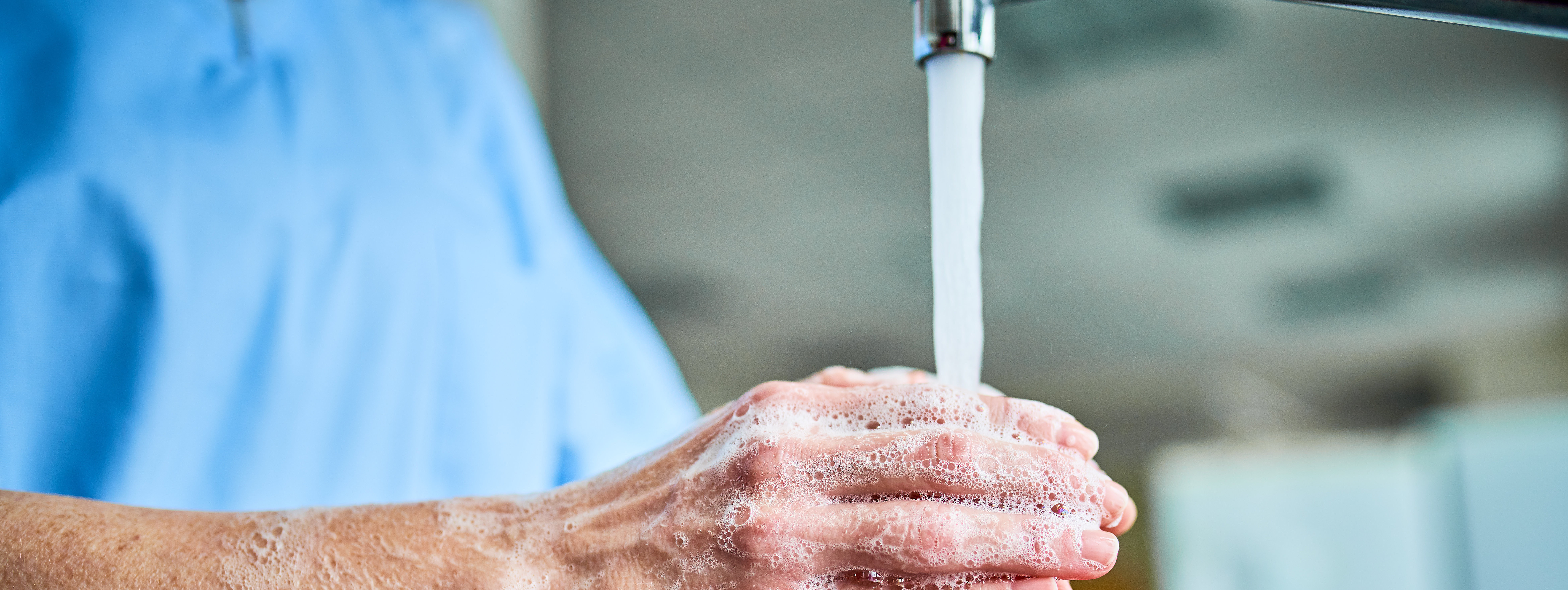 Hände werden unter fließendem Wasser mit Seife eingeseift und abgespült.