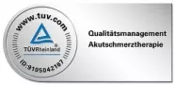 Rundes TÜV Rheinland Prüfzeichen mit blauem Dreieck und Text 'Qualitätsmanagement Akutschmerztherapie'