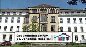 Fassade eines historischen Gebäudes mit Schild 'Gesundheitszentrum St. Johannes-Hospital' davor