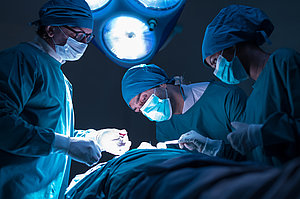 Drei Chirurgen in Operationskleidung führen eine Operation unter hellem OP-Licht durch