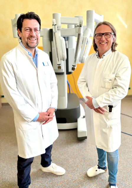 Zwei Personen in weißen Kitteln stehen vor einem medizinischen Roboter mit mehreren Armen