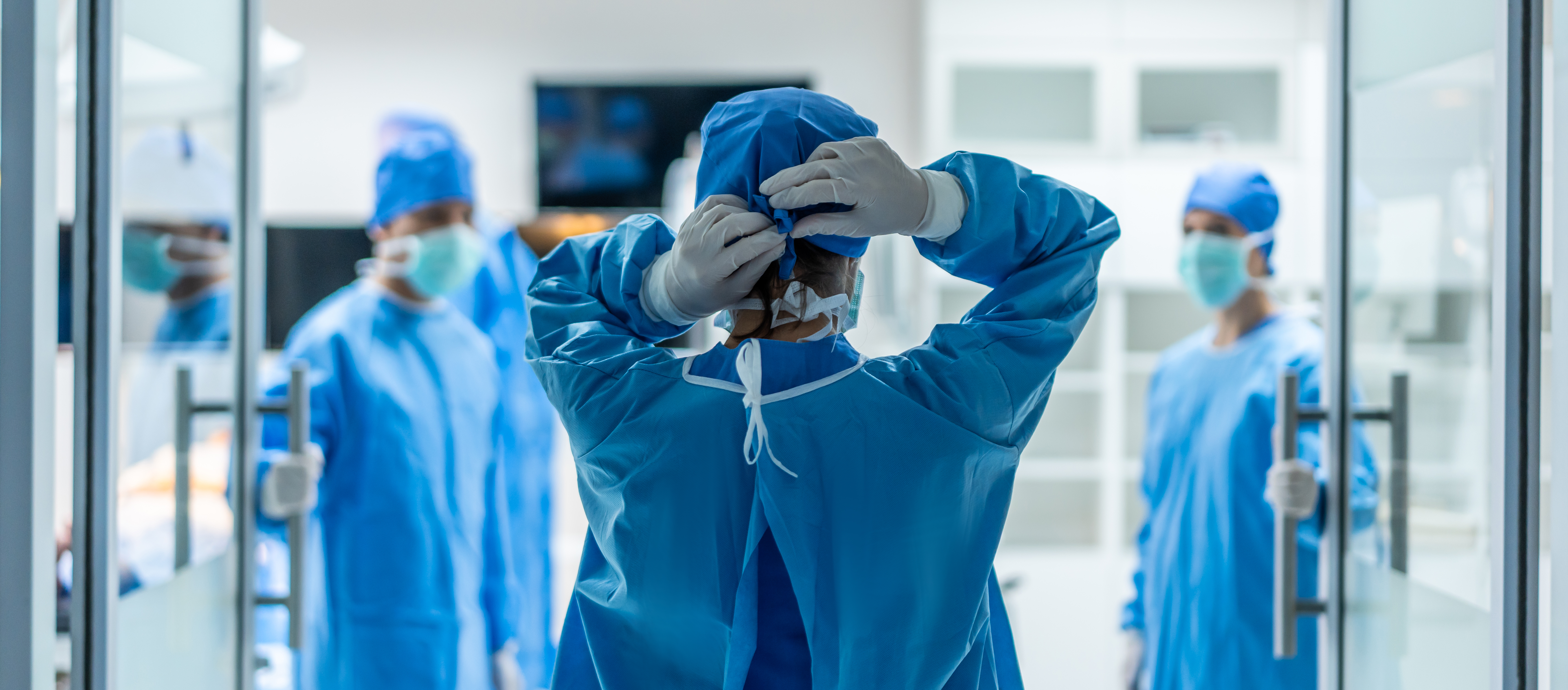 Person in Schutzkleidung bindet im Krankenhausflur den Knoten am Haarschutz zusammen